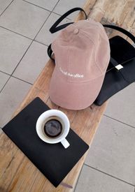 Pink Baseball Cap A Shoulder Bag A Note Pad And A Cup Of Coffee Lying On A Wooden Bench