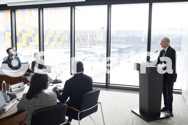 Elderly Business Man Standing Near Podium In Front Of People